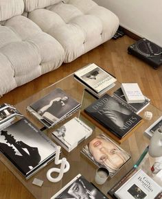 a glass coffee table topped with lots of books on top of a hard wood floor