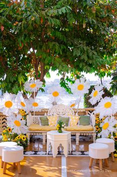 an outdoor seating area with yellow and white flowers on the bench, tables and chairs