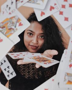 a woman holding playing cards in front of her face and surrounded by other playing cards