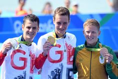 three men standing next to each other holding gold medals