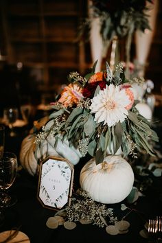 an arrangement of flowers and pumpkins on a black table cloth with place cards for guests