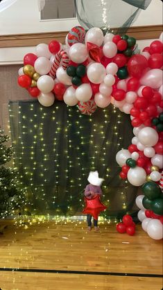 a person standing under a bunch of balloons in front of a christmas tree on a wooden floor