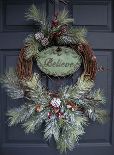 a christmas wreath with pine cones and berries hanging from the front door to spell believe