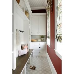 a long hallway with white cabinets and red walls, along with a bench in front of the window