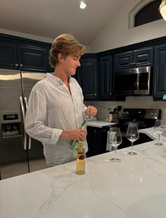 a man standing at the kitchen counter pouring wine into two glasses on top of it