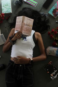 a woman laying on the ground with a book in her hand and other items around her