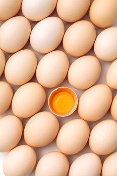 an egg is surrounded by several eggs and a small bowl with orange liquid in it