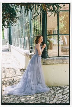 a woman in a blue dress leaning against a pole