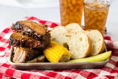 a tray filled with meat, bread and pickles next to two glasses of beer