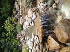 a small waterfall in the middle of a garden with rocks and water flowing from it