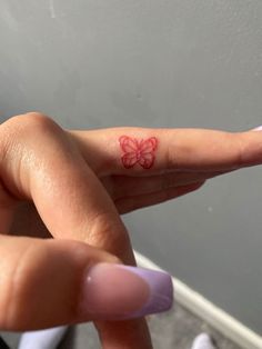 a woman's finger with a red butterfly tattoo on it