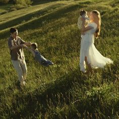 a woman in a white dress holding a baby while standing next to two other people