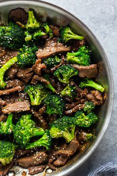 beef and broccoli stir fry in a pan with sesame seeds on the side