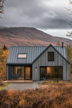 a house with a metal roof in the middle of a field and mountains behind it