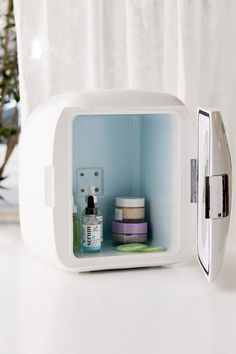 an open refrigerator sitting on top of a table next to a potted plant and bottle