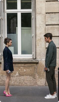 a man and woman standing in front of a window talking to each other on the street