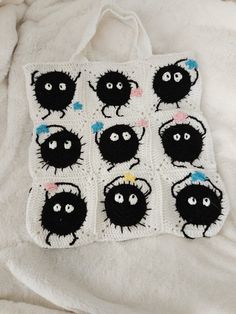 a crocheted bag with black cats on it sitting on a white blanket,