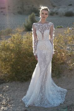 a woman in a white wedding dress standing on the sand with her arms behind her back