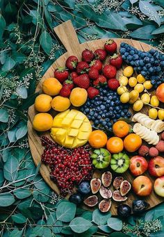 a wooden plate topped with lots of different types of fruits and vegetables next to green leaves