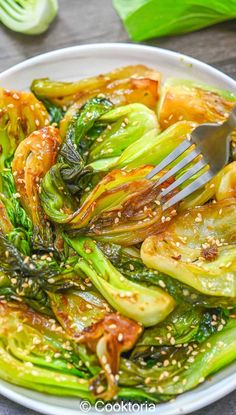 stir fried vegetables with sesame seeds and seasoning in a white bowl on a wooden table