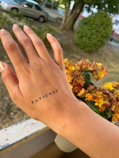 a person's hand with the word patience tattooed on their left wrist, in front of some flowers