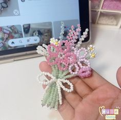 a hand holding a small flower brooch in it's left hand, next to a computer screen