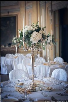 an elegant centerpiece with white flowers and greenery sits on a table in the middle of a formal dining room