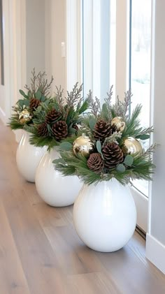 three white vases with pine cones and greenery in them on a wooden floor