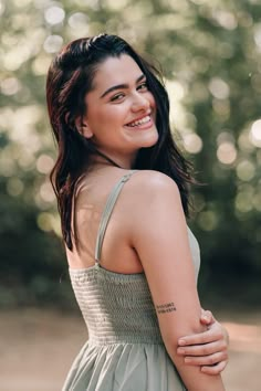 a woman in a green dress smiling and looking at the camera with trees behind her