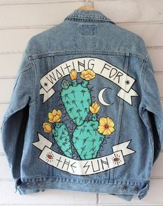 a denim jacket with an image of a cactus and flowers on it hanging up against a white brick wall