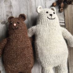 two knitted teddy bears sitting next to each other on a wooden surface with pine cones