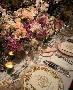 the table is set with many plates and silverware, flowers in glass vases