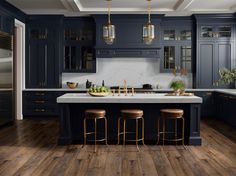 a kitchen with dark blue cabinets and wooden flooring, two stools on the island