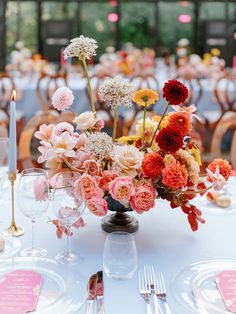 an arrangement of flowers in a vase on top of a table with place cards and silverware