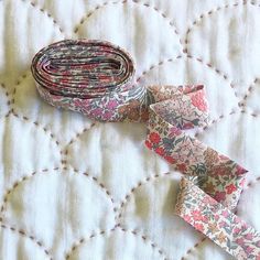 two pieces of fabric sitting on top of a quilted tablecloth covered in white and pink flowers