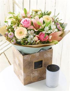 a bouquet of flowers sitting in a box next to an empty cup on a table