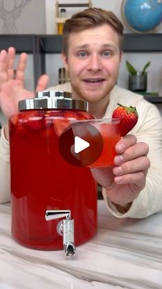 a man is holding up a red drink in front of a glass with a strawberries on it