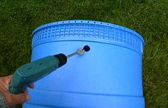 a person is using a drill to paint a blue barrel on the ground with green grass