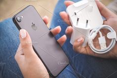 a woman is holding an iphone in her hand and plugged into the charger