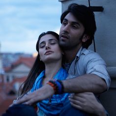 a man and woman embracing each other in front of a clock tower with buildings in the background