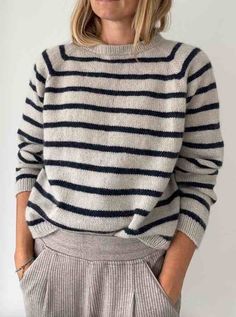 a woman wearing a striped sweater and pleated pants with her hands in her pockets