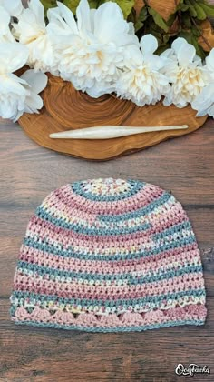 a crocheted hat sitting on top of a wooden table next to white flowers