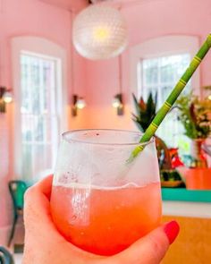 a person holding a drink with a green straw in it's hand and pink walls