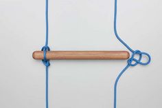 a piece of wood hanging from a blue string on a white wall with a wooden stick attached to it