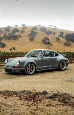 a grey porsche parked on top of a dirt field