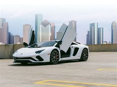 a white sports car with open doors parked in front of a cityscape background