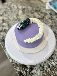 a purple cake with white frosting and a green car on top sitting on a counter