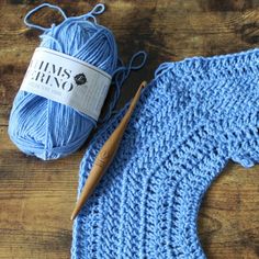 a blue knitted sweater with a crochet hook and ball of yarn next to it