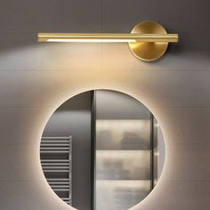 a bathroom with a round mirror on the wall and a gold light fixture above it