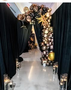 an entrance decorated with black and gold balloons, candles and streamers for a party